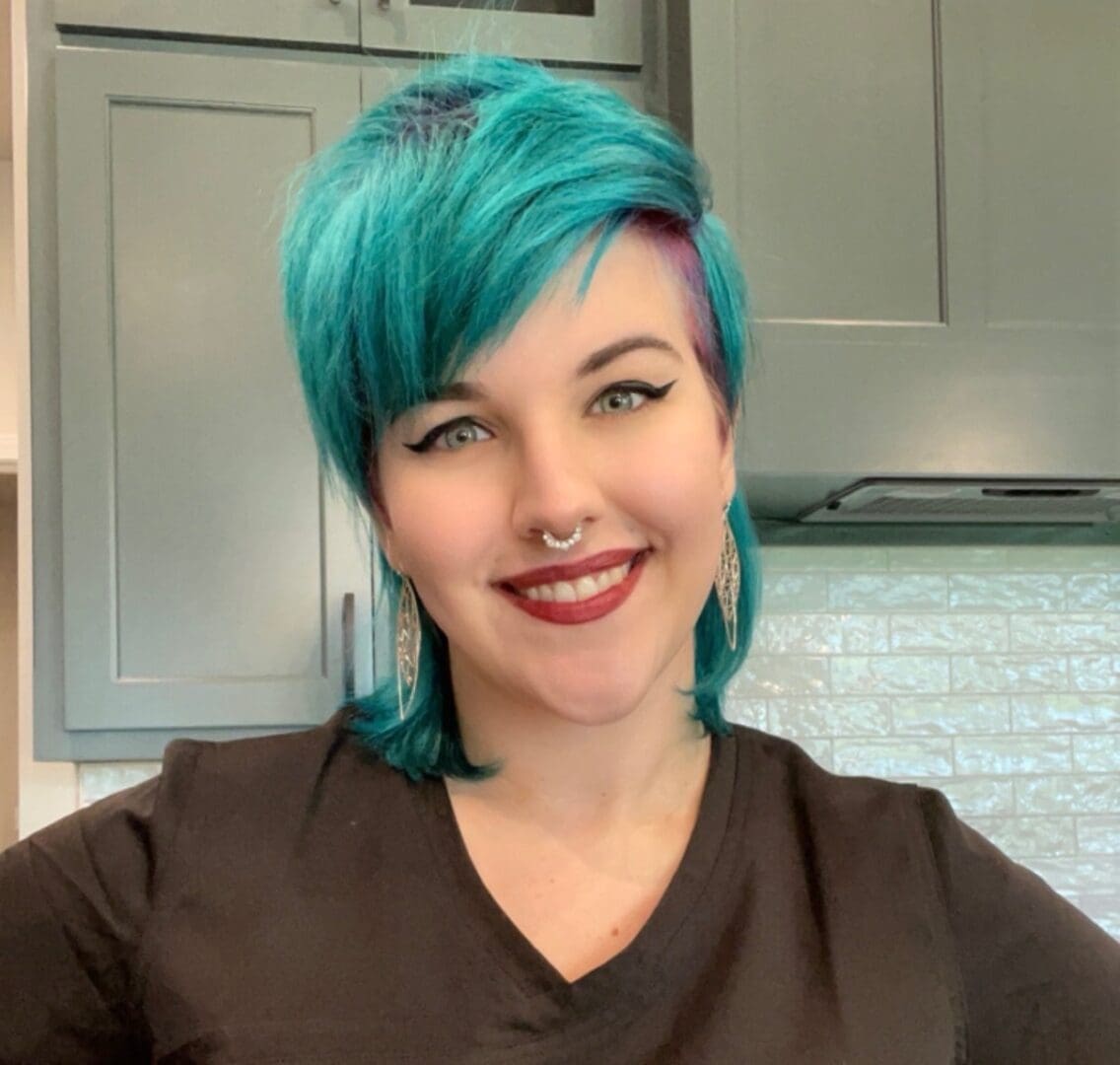 A woman with blue hair is smiling for the camera.